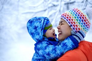 An Asian woman mother and her baby boy are playing in a snowy park in winter