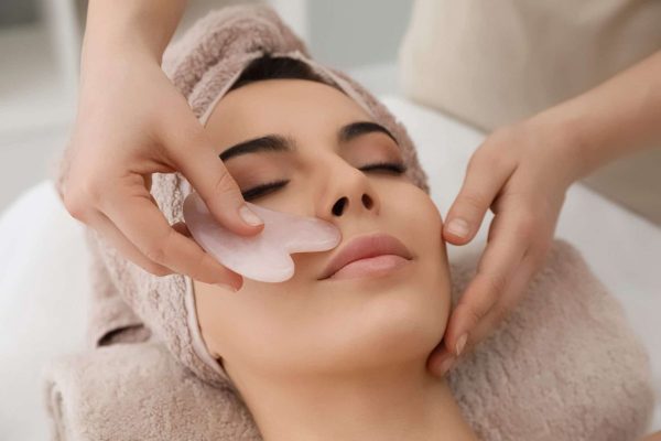 Rose quartz gua sha massage receiving facial massage with gua sha tool in beauty salon
